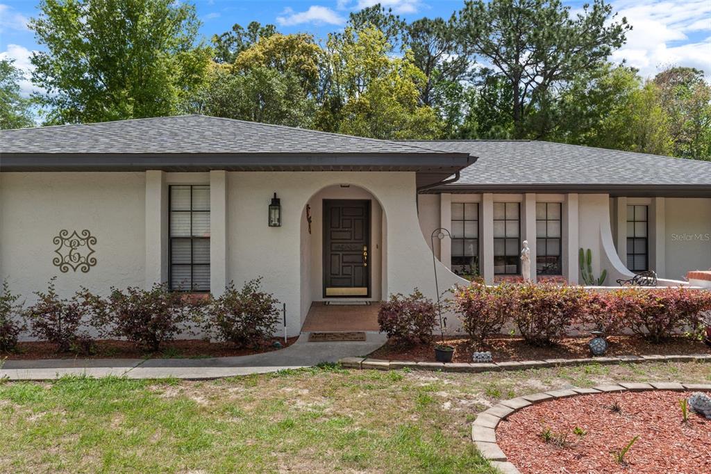 A single-story house with a stucco exterior, arched entryway, and a dark shingled roof — 5 MANGROVE COURT S, HOMOSASSA, FL