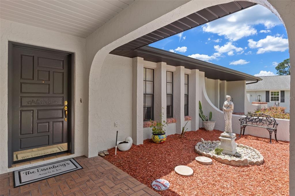 A covered entryway features a dark front door, a statue, and red mulch landscaping — 5 MANGROVE COURT S, HOMOSASSA, FL