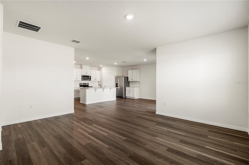 An open-concept living area with wood-look flooring leads to a kitchen with white cabinetry — 1699 THREE BARS ROAD, KISSIMMEE, FL