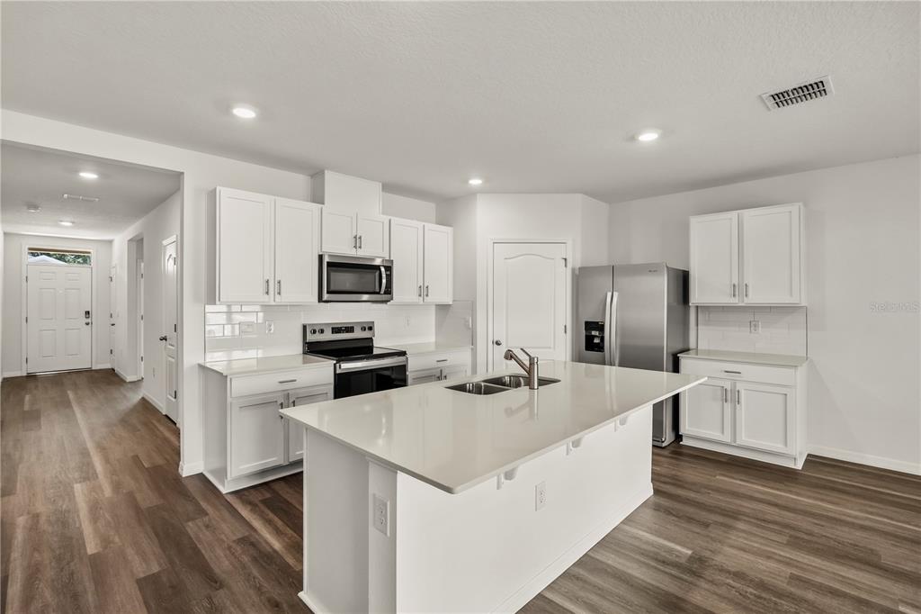 A modern kitchen features white cabinetry, stainless steel appliances, a center island, and wood-look flooring — 1699 THREE BARS ROAD, KISSIMMEE, FL
