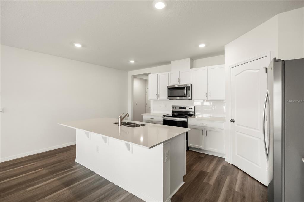 A kitchen features a white island, white cabinetry, stainless steel appliances, and wood-look flooring — 1699 THREE BARS ROAD, KISSIMMEE, FL