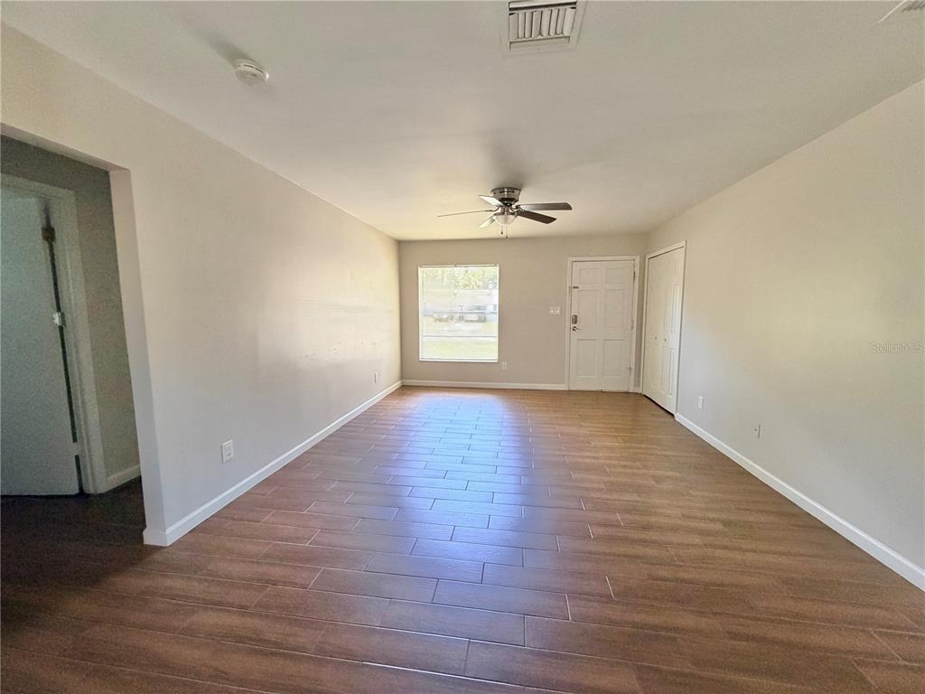 An empty living room features light-colored walls, wood-look tile flooring, and a ceiling fan — 130 S BULOVA DRIVE, APOPKA, FL