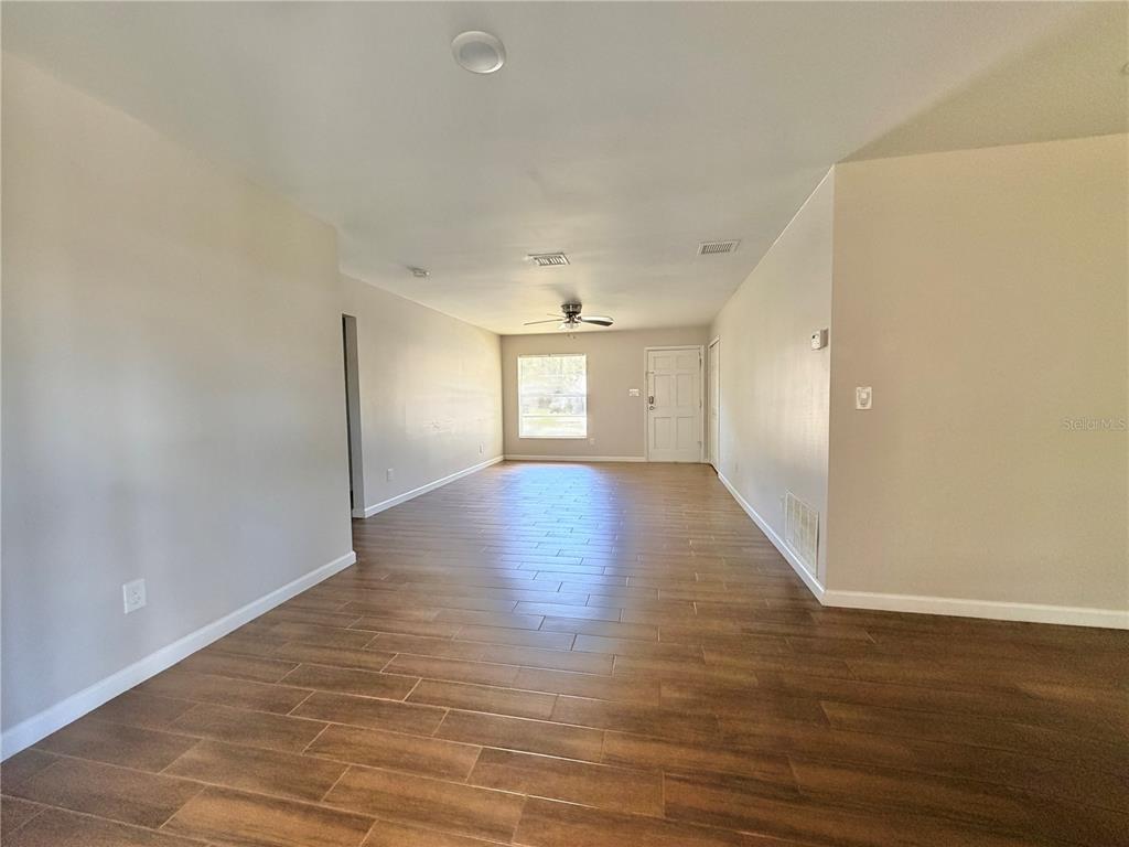 An empty living room features light-colored walls, wood-look tile flooring, and a ceiling fan — 130 S BULOVA DRIVE, APOPKA, FL