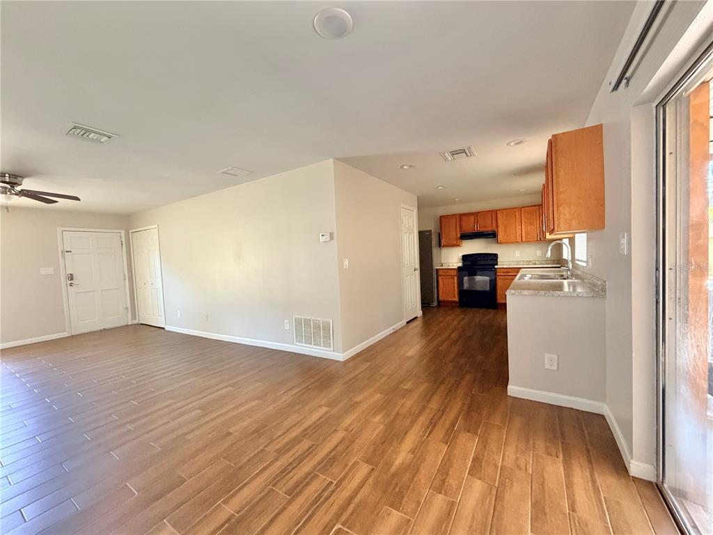 An open-concept living area with wood-look tile flooring leads into a kitchen with wooden cabinets — 130 S BULOVA DRIVE, APOPKA, FL