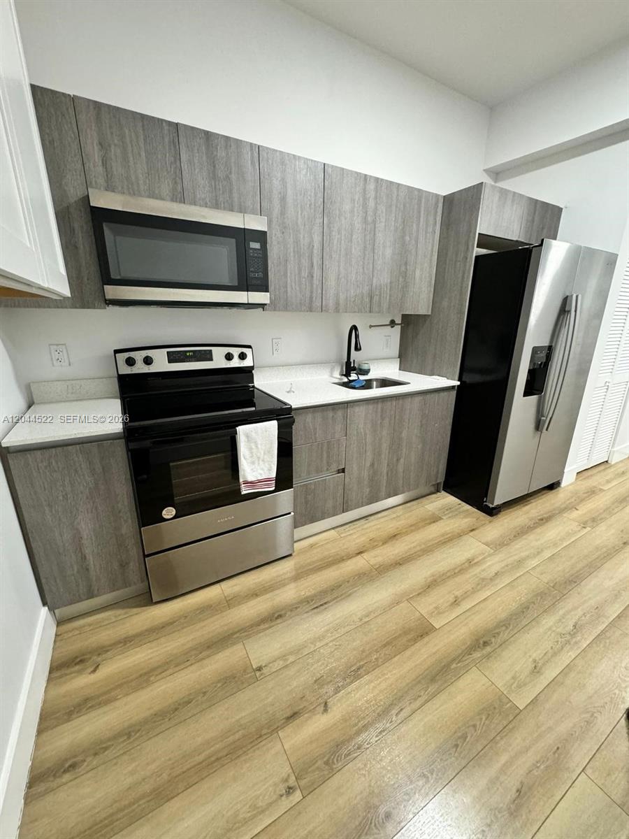 A modern kitchen features gray wood-grain cabinets, stainless steel appliances, and light wood flooring — 1021 NW 1st St # 204, Miami FL 33128, MIAMI, FL