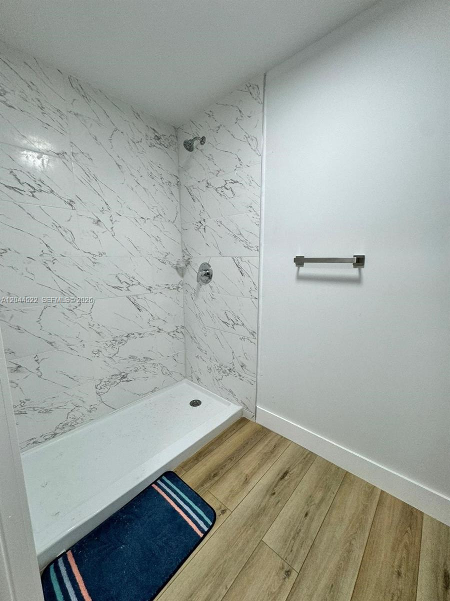 A walk-in shower with marble-patterned tile walls and a light wood-look floor — 1021 NW 1st St # 204, Miami FL 33128, MIAMI, FL