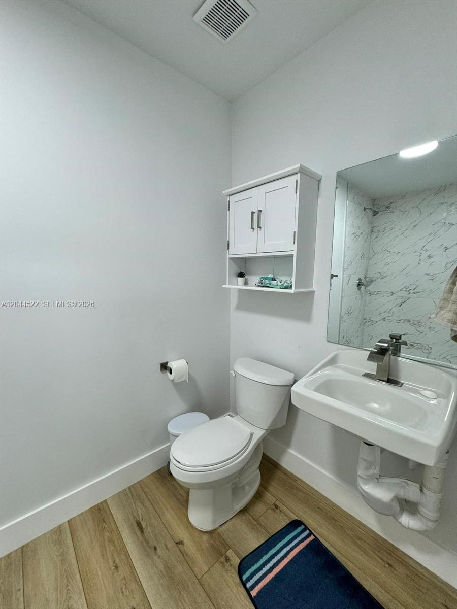 A bathroom features a white toilet, a wall-mounted sink, a cabinet, and wood-look flooring — 1021 NW 1st St # 204, Miami FL 33128, MIAMI, FL