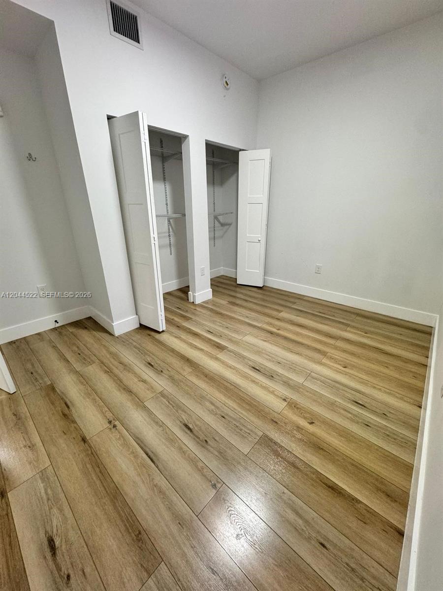 An empty room features light wood-look flooring, white walls, and two open closets — 1021 NW 1st St # 204, Miami FL 33128, MIAMI, FL