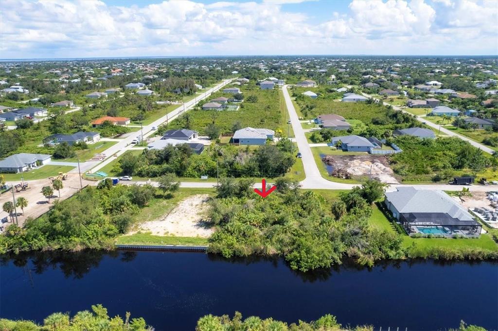 An aerial view shows a vacant, overgrown waterfront lot marked by a red arrow — 13391 CHENILLE DRIVE, PORT CHARLOTTE, FL