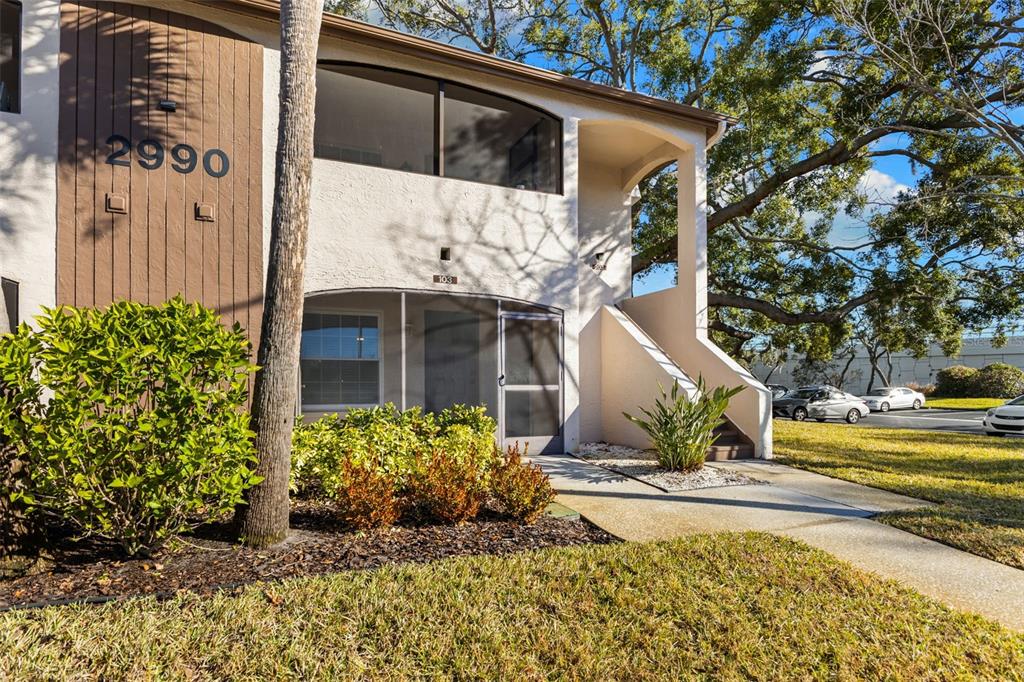 A two-story apartment building exterior features a screened-in ground floor entrance and upper balcony — 2990 BONAVENTURE CIRCLE UNIT 103, PALM HARBOR, FL