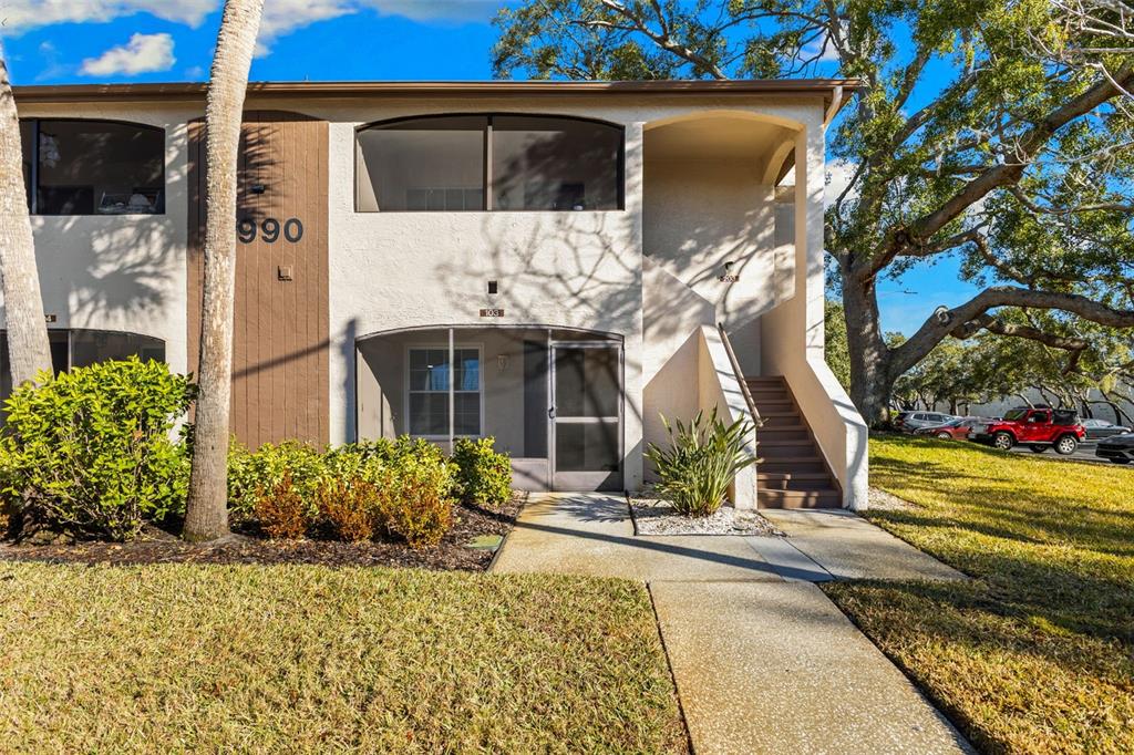 A two-story apartment building exterior features a ground-floor screened patio and an outdoor staircase — 2990 BONAVENTURE CIRCLE UNIT 103, PALM HARBOR, FL
