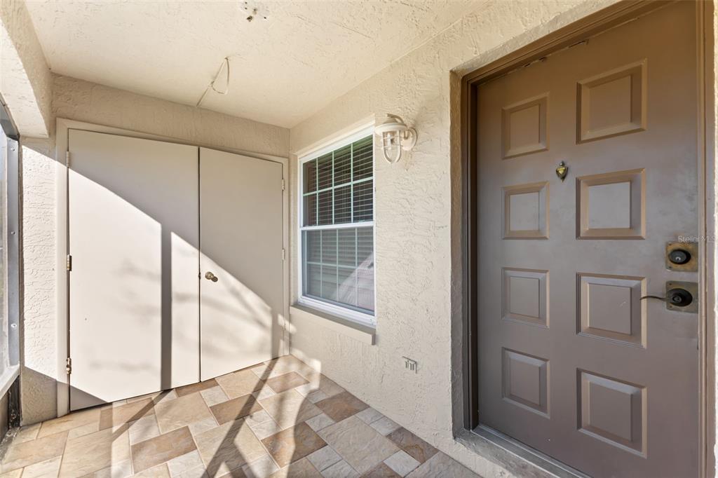 A covered entryway features a brown front door, a storage closet, and tiled flooring — 2990 BONAVENTURE CIRCLE UNIT 103, PALM HARBOR, FL