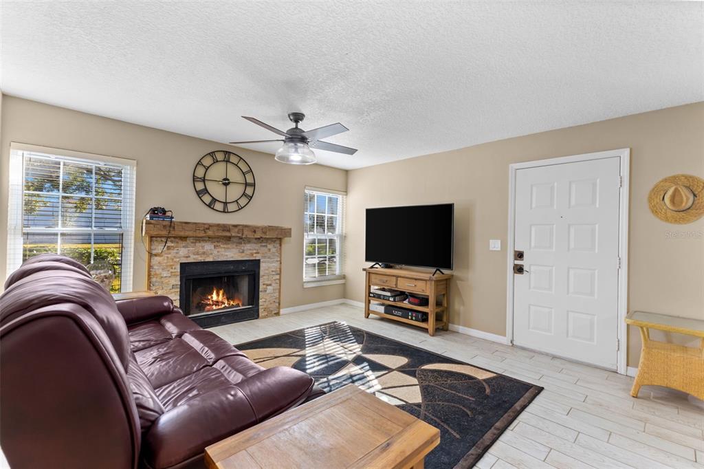 A living room features a stone fireplace, a television on a stand, and a leather sofa — 2990 BONAVENTURE CIRCLE UNIT 103, PALM HARBOR, FL