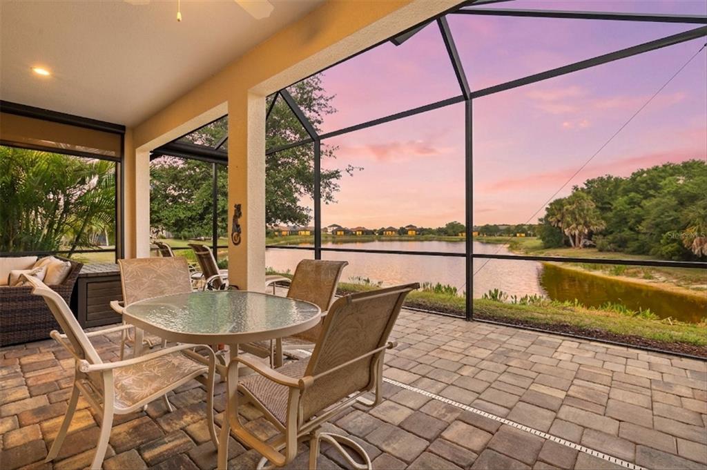 A screened-in patio with outdoor furniture overlooks a lake at sunset — 11876 HUNTERS CREEK ROAD, VENICE, FL