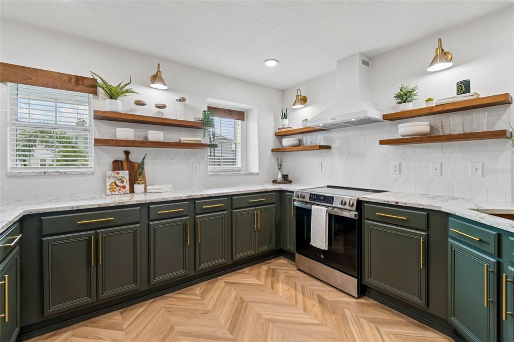 A kitchen features dark green cabinets, wood floating shelves, white tile backsplash, and herringbone flooring — 504 WHEATON TRENT PLACE, TAMPA, FL