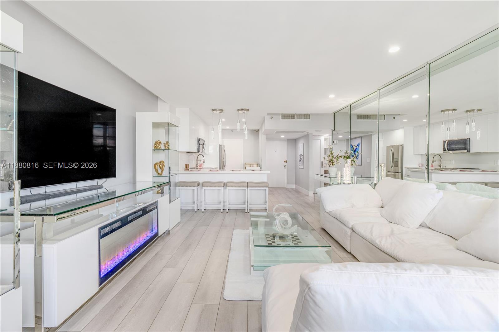 A modern white kitchen features a breakfast bar with three stools and mirrored walls — 100 Lincoln Rd # 323, Miami Beach FL 33139, MIAMI BEACH, FL