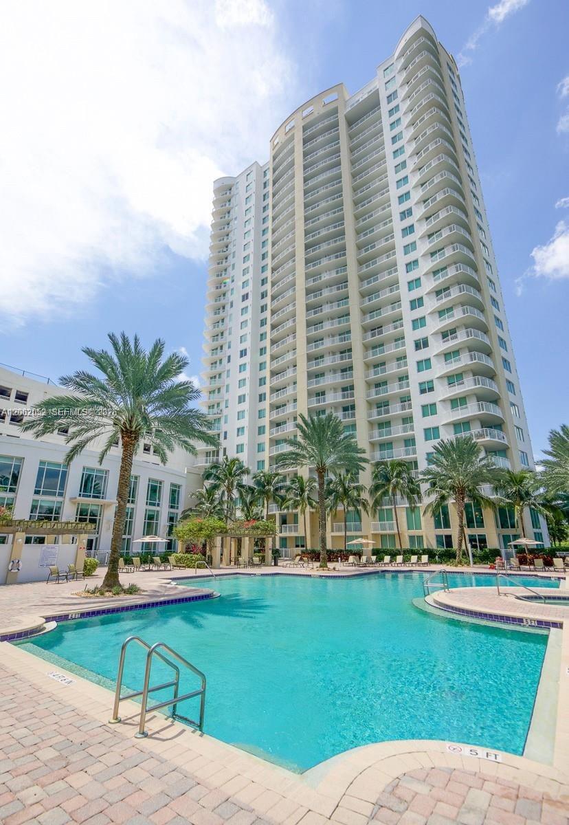 A tall residential high-rise building stands behind a swimming pool with palm trees — 1745 E Hallandale Beach Blvd # 306W, Hallandale Beach FL 33009, HALLANDALE BEACH, FL