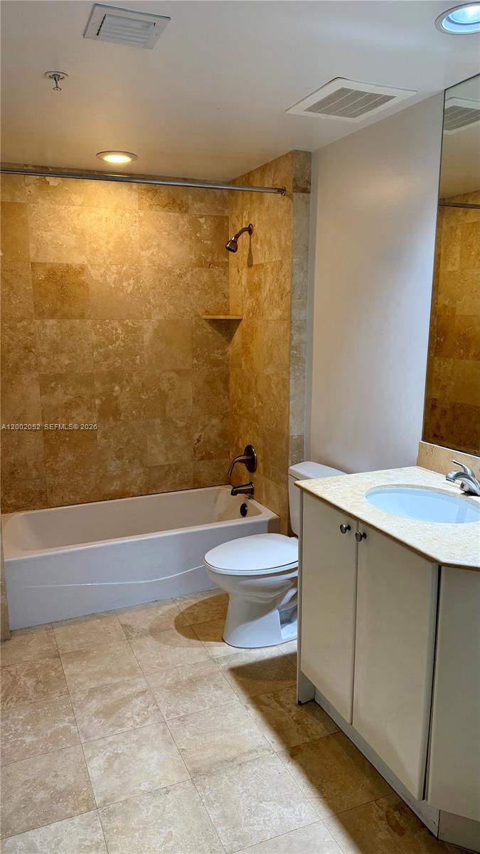 A bathroom features a white bathtub, a toilet, and a vanity with stone-look tile flooring — 1745 E Hallandale Beach Blvd # 306W, Hallandale Beach FL 33009, HALLANDALE BEACH, FL