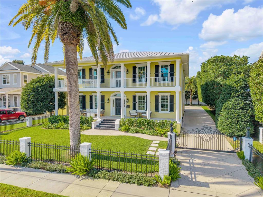 A two-story yellow house features a double-decker porch, white columns, and a gated driveway — 1212 S RIVERSIDE DRIVE, NEW SMYRNA BEACH, FL