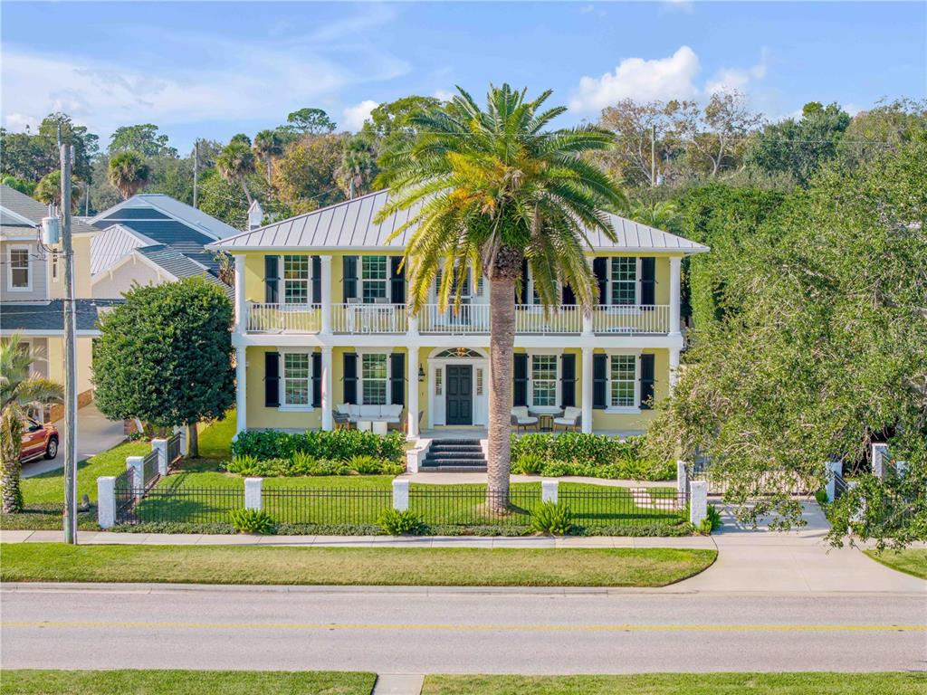 A two-story yellow house with a metal roof and a large palm tree in front — 1212 S RIVERSIDE DRIVE, NEW SMYRNA BEACH, FL