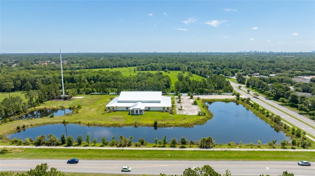 An aerial view shows a large white building surrounded by a pond and green fields — 4015 S WILLIAMSON BOULEVARD, PORT ORANGE, FL