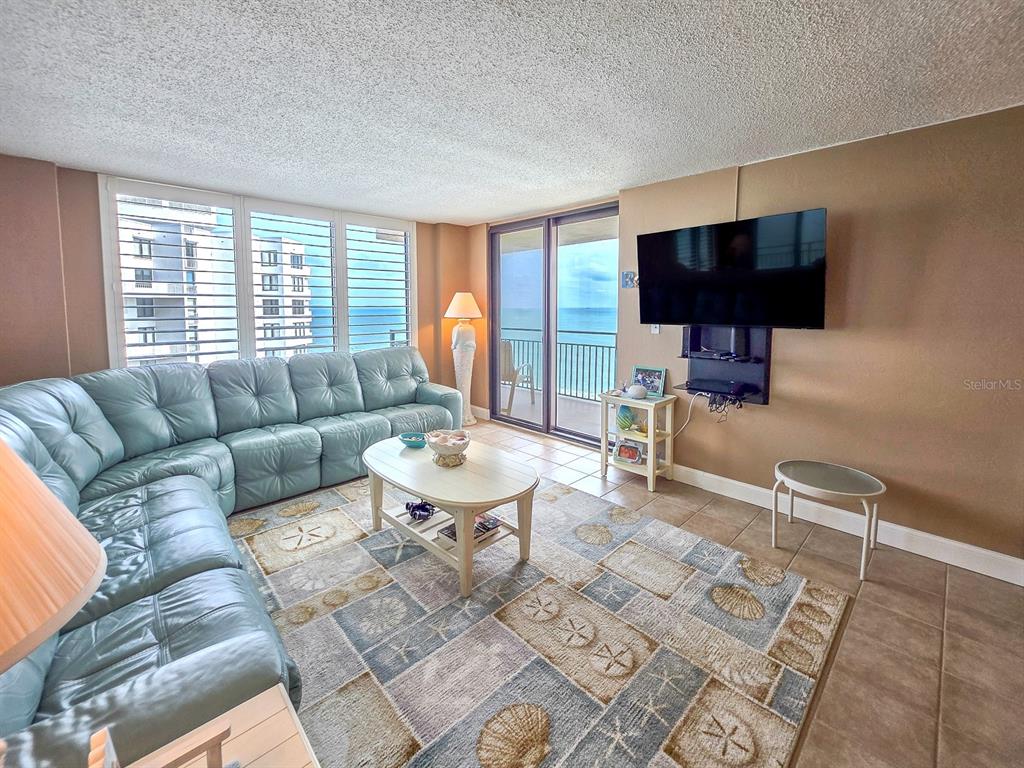 A living room features a blue leather sectional, a coastal rug, and a balcony view — 3051 S. ATLANTIC AVENUE UNIT 1805, DAYTONA BEACH SHORES, FL