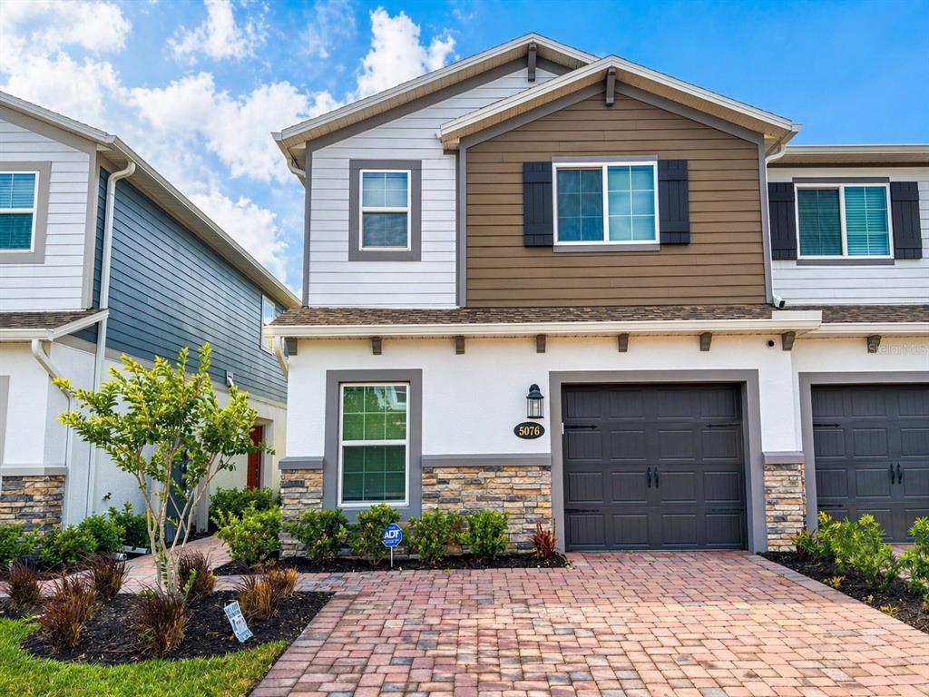 A two-story townhouse with a stone-accented facade, a single-car garage, and a brick paver driveway — 5076 RAIN SHADOW DRIVE, ST CLOUD, FL
