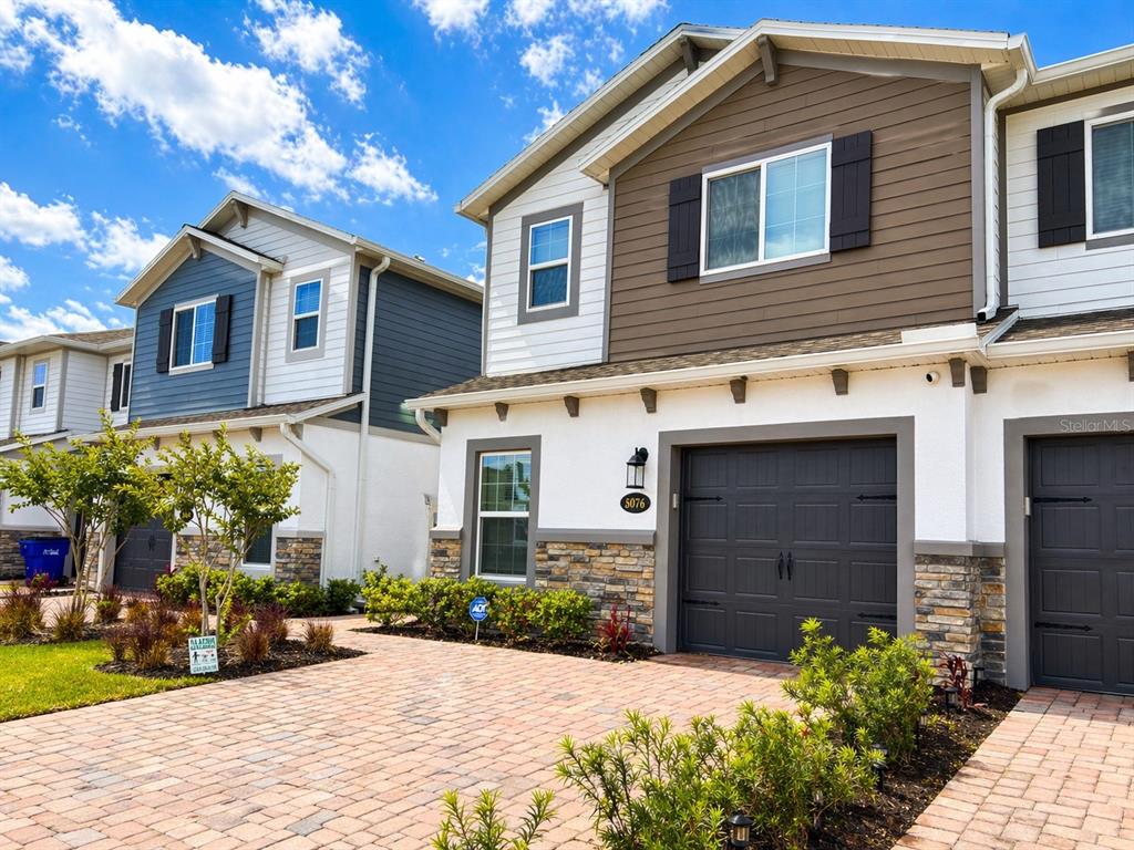 A two-story townhouse with a stone-accented facade, a dark garage door, and a brick driveway — 5076 RAIN SHADOW DRIVE, ST CLOUD, FL