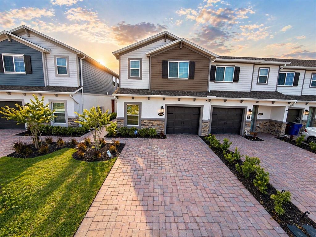 A two-story townhouse with a brick paver driveway and an attached garage at sunset — 5076 RAIN SHADOW DRIVE, ST CLOUD, FL