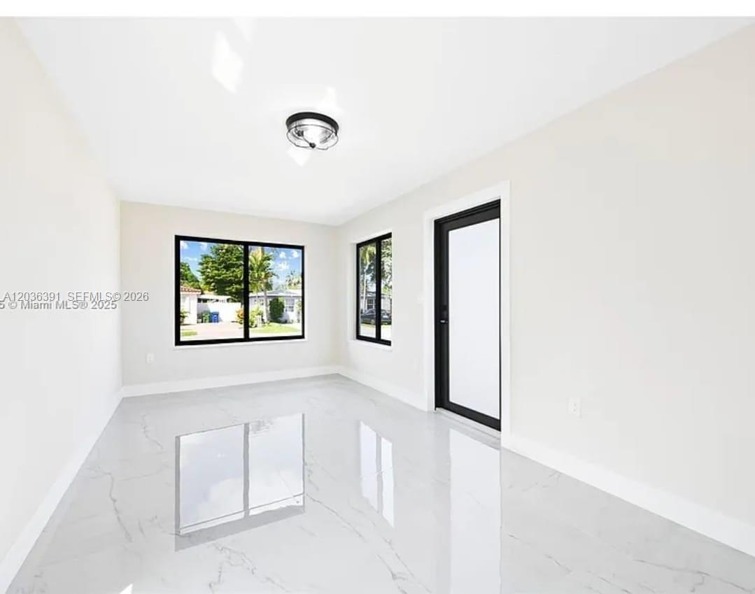 A bright, empty room features white marble-look tile flooring, white walls, and black-framed windows — 721 SW 5th Ct # 0, Hallandale Beach FL 33009, HALLANDALE BEACH, FL