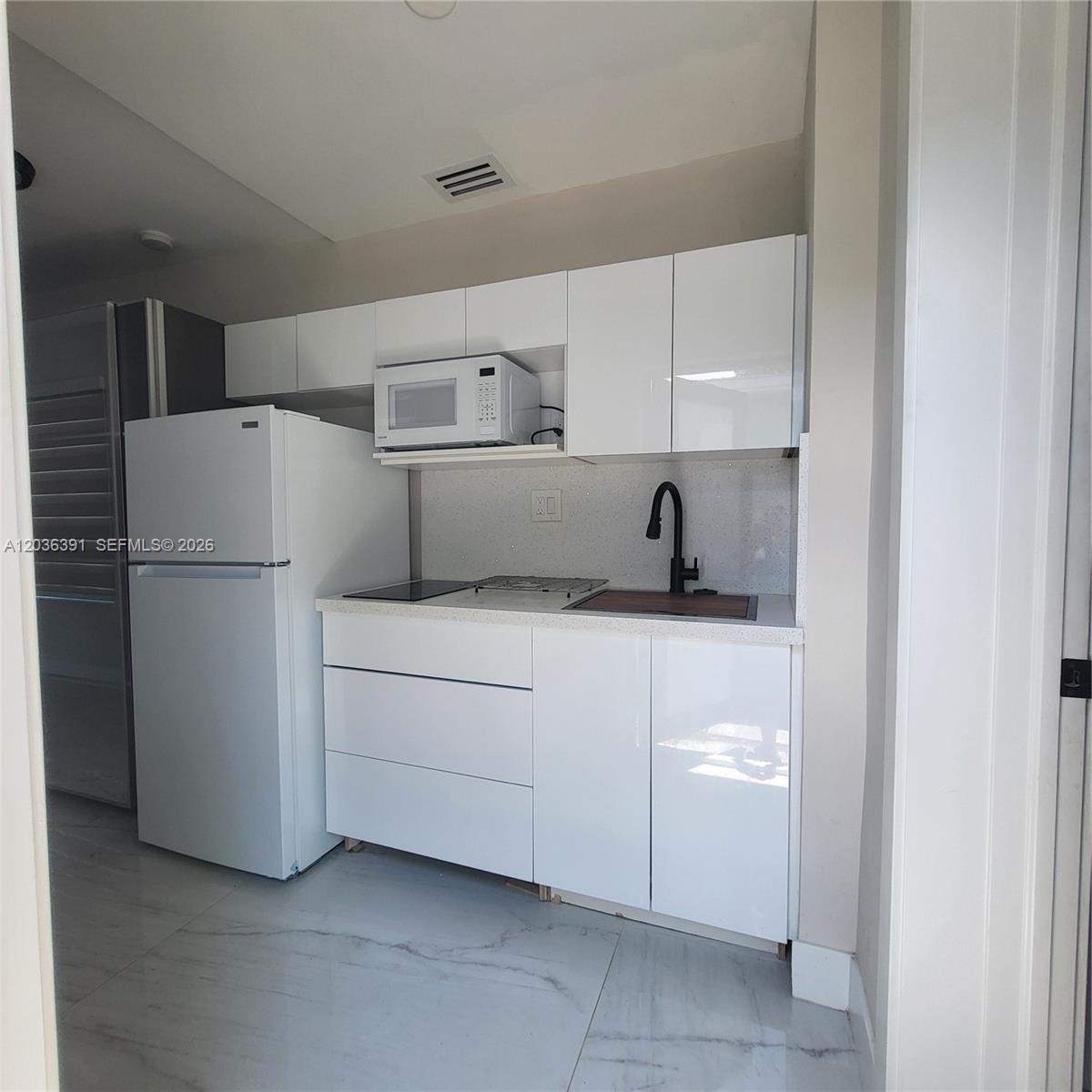 A small kitchen features white glossy cabinets, a white refrigerator, and a black faucet — 721 SW 5th Ct # 0, Hallandale Beach FL 33009, HALLANDALE BEACH, FL