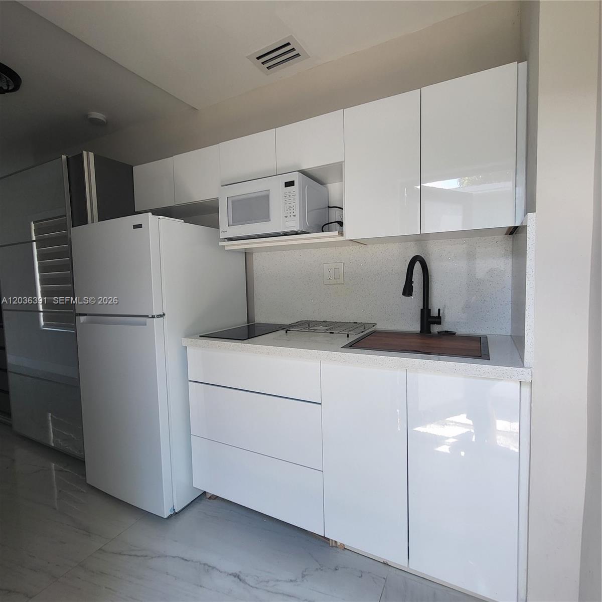 A small kitchen features white glossy cabinets, a white refrigerator, and a black faucet — 721 SW 5th Ct # 0, Hallandale Beach FL 33009, HALLANDALE BEACH, FL