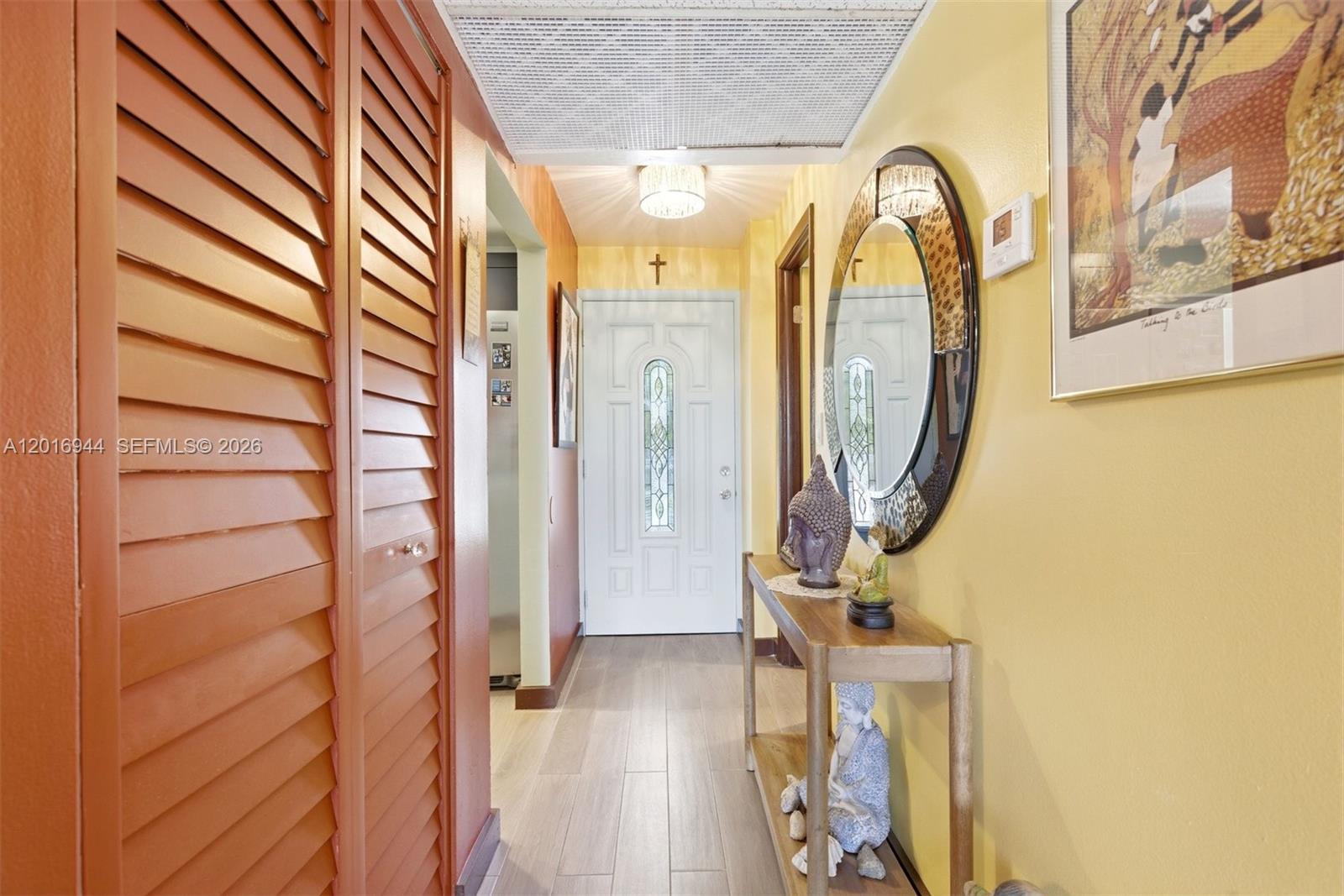 A hallway features a louvered closet door, a console table with statues, and yellow walls — 111 Royal Park Dr # 2E, Oakland Park FL 33309, OAKLAND PARK, FL