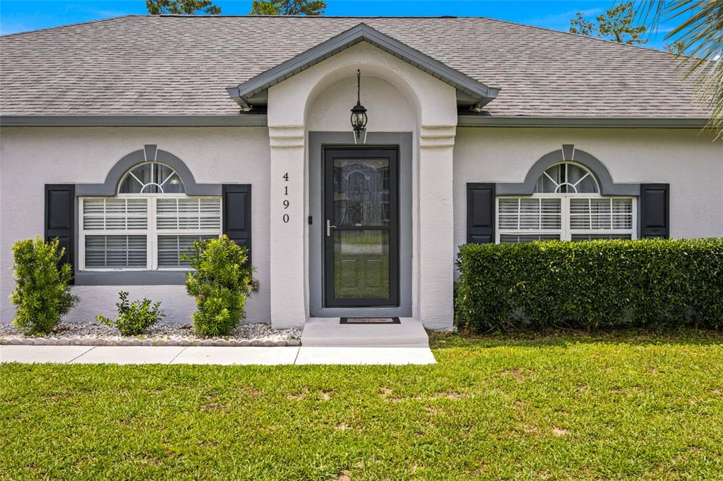 The exterior of a single-story house features a gray arched entryway, shutters, and landscaping — 4190 SW 110TH LANE, OCALA, FL