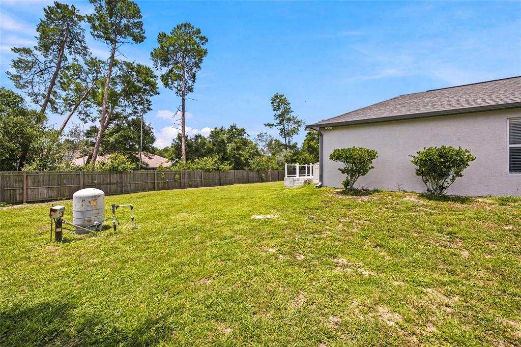 A grassy backyard features a wooden fence, a white house exterior, and a water softener — 4190 SW 110TH LANE, OCALA, FL
