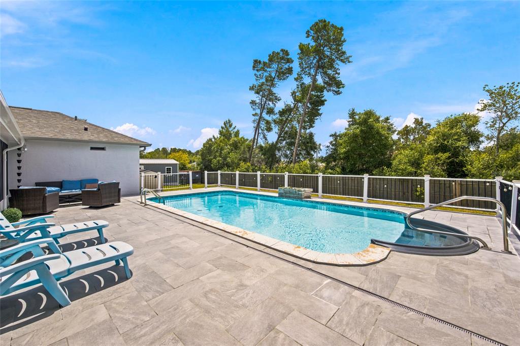 A backyard features a rectangular swimming pool with a spa, stone patio, and white fencing — 4190 SW 110TH LANE, OCALA, FL