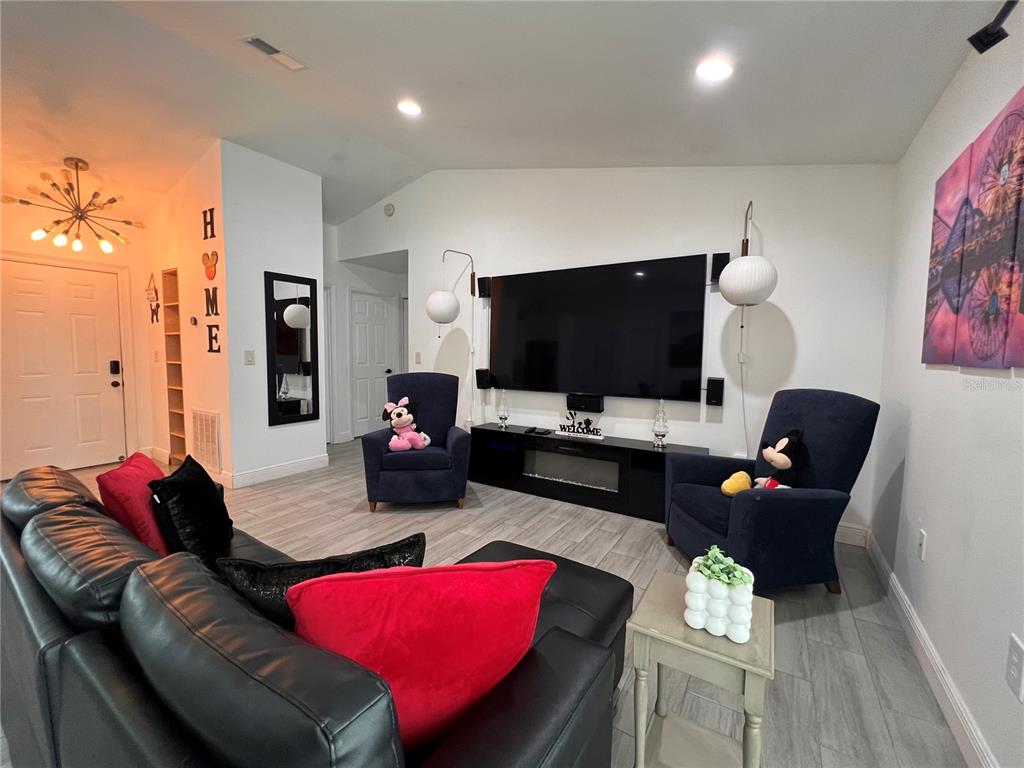 A living room and dining area feature light wood-look tile flooring and a large television — 638 BALDWIN DRIVE, KISSIMMEE, FL