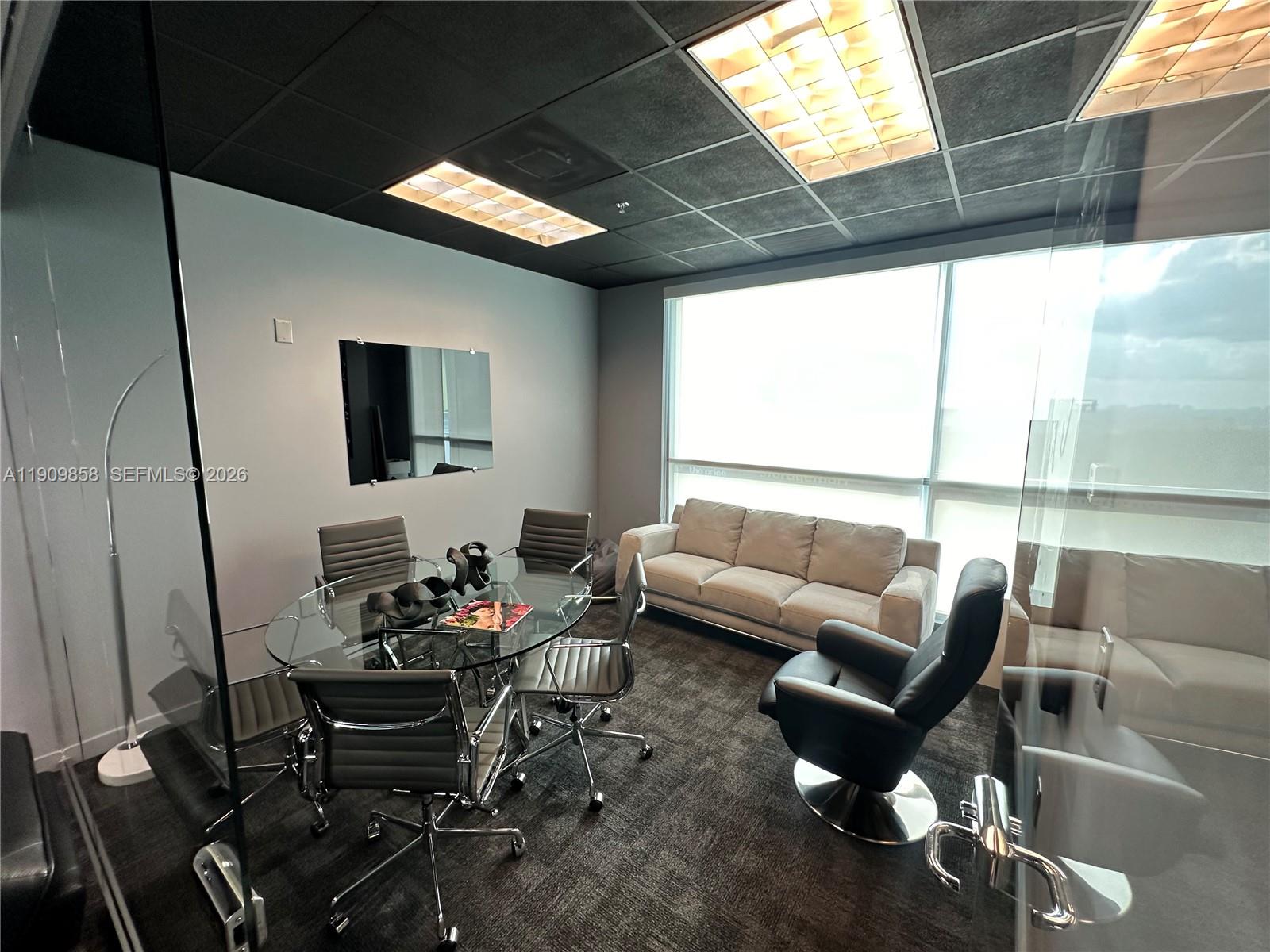 A modern office meeting room features a glass table, gray chairs, a sofa, and dark carpeting — 175 SW 7 ST # 1101, Miami FL 33130, MIAMI, FL