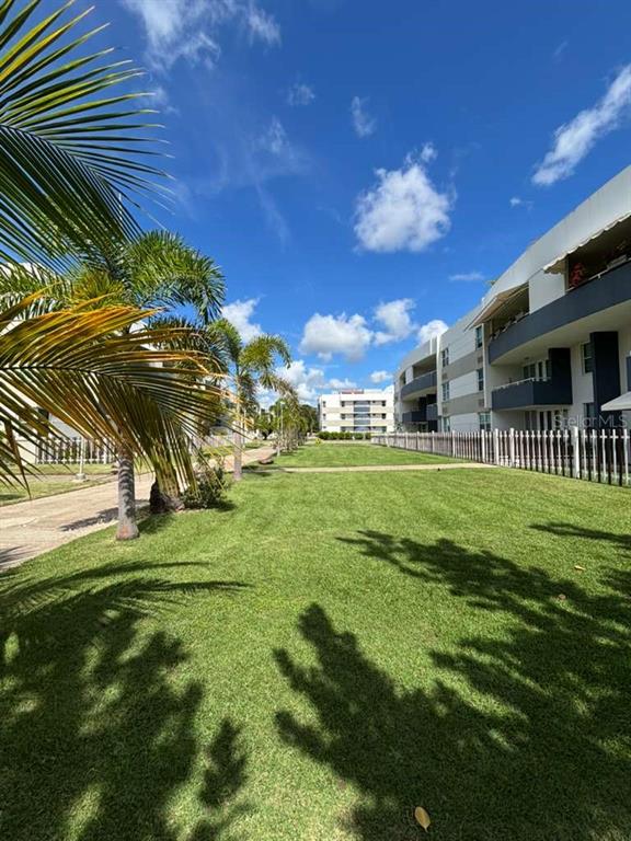 A grassy courtyard sits between two multi-story apartment buildings under a bright blue sky — PH 1-A ARROYO BEACH RESORT UNIT PH1-A, ARROYO, PR