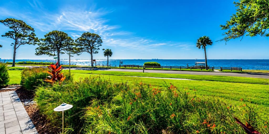 A grassy lawn with trees and plants overlooks a body of water under a blue sky — 7927 LONGBAY BOULEVARD, SARASOTA, FL