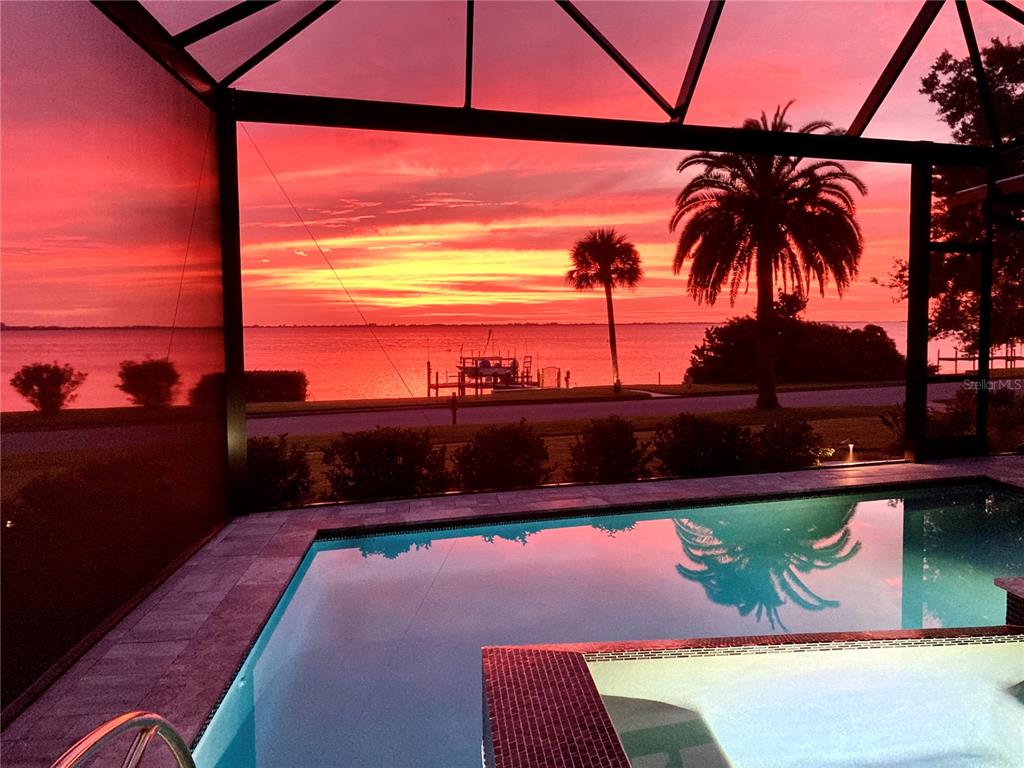 A swimming pool and spa overlook a waterfront sunset view from a screened-in patio — 7927 LONGBAY BOULEVARD, SARASOTA, FL