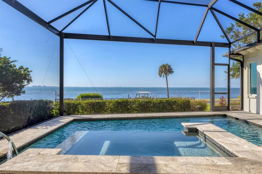 A screened-in pool and spa overlook a body of water with a palm tree — 7927 LONGBAY BOULEVARD, SARASOTA, FL