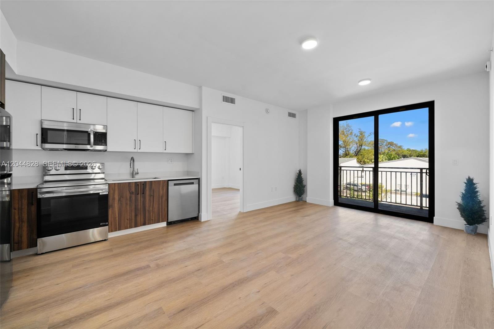 A kitchen with white and wood cabinets opens to a living area with a balcony — 2479 NE 192nd St # 308, Miami FL 33180, MIAMI, FL