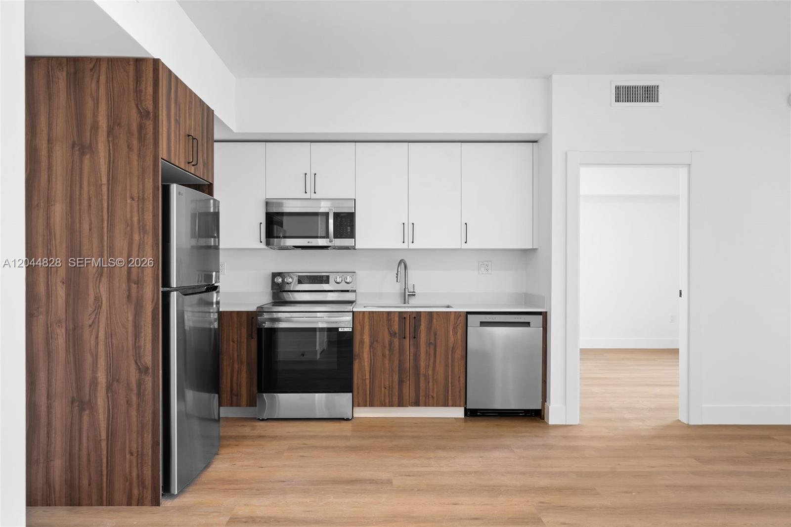 A modern kitchen features wood-grain lower cabinets, white upper cabinets, and stainless steel appliances — 2479 NE 192nd St # 308, Miami FL 33180, MIAMI, FL