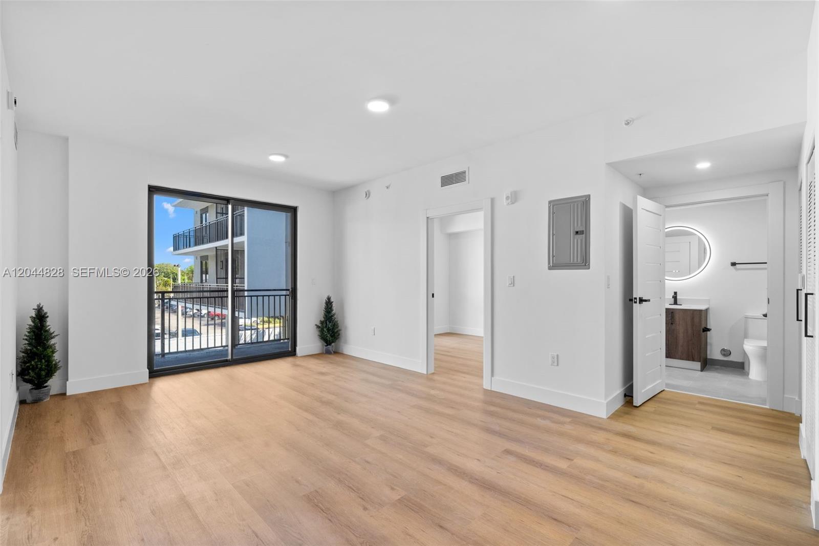 An empty room features light wood-look flooring, white walls, a sliding glass door, and a bathroom — 2479 NE 192nd St # 308, Miami FL 33180, MIAMI, FL