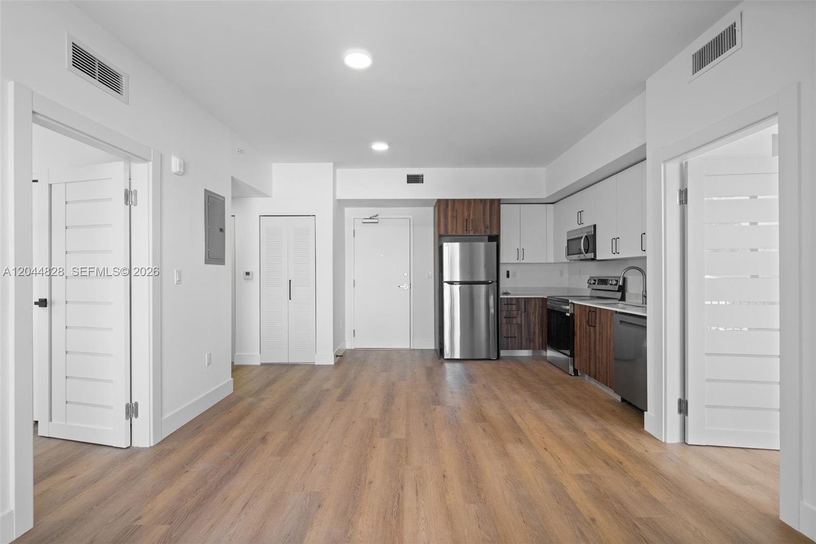 A modern kitchen with stainless steel appliances and wood-look flooring opens into a living area — 2479 NE 192nd St # 308, Miami FL 33180, MIAMI, FL