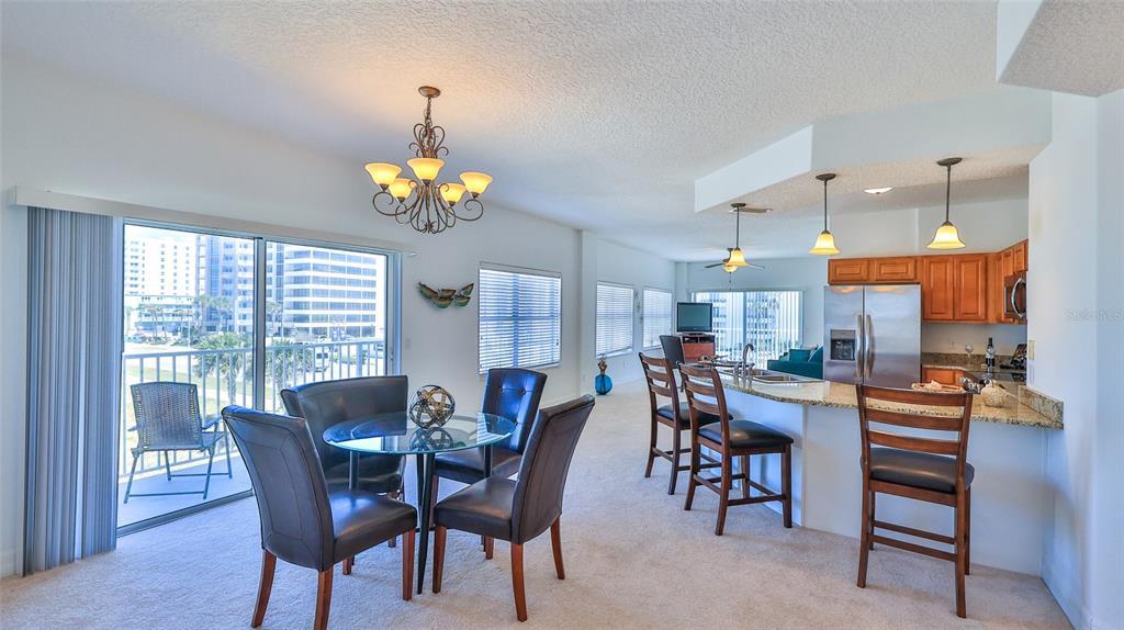 A dining area and kitchen with a breakfast bar, stainless steel appliances, and balcony access — 3756 S ATLANTIC AVENUE UNIT 201, DAYTONA BEACH, FL