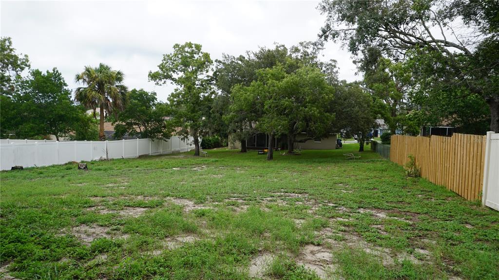 A large, grassy backyard features mature trees, a white vinyl fence, and a wooden fence — 7317 LITTLE ROAD, NEW PORT RICHEY, FL