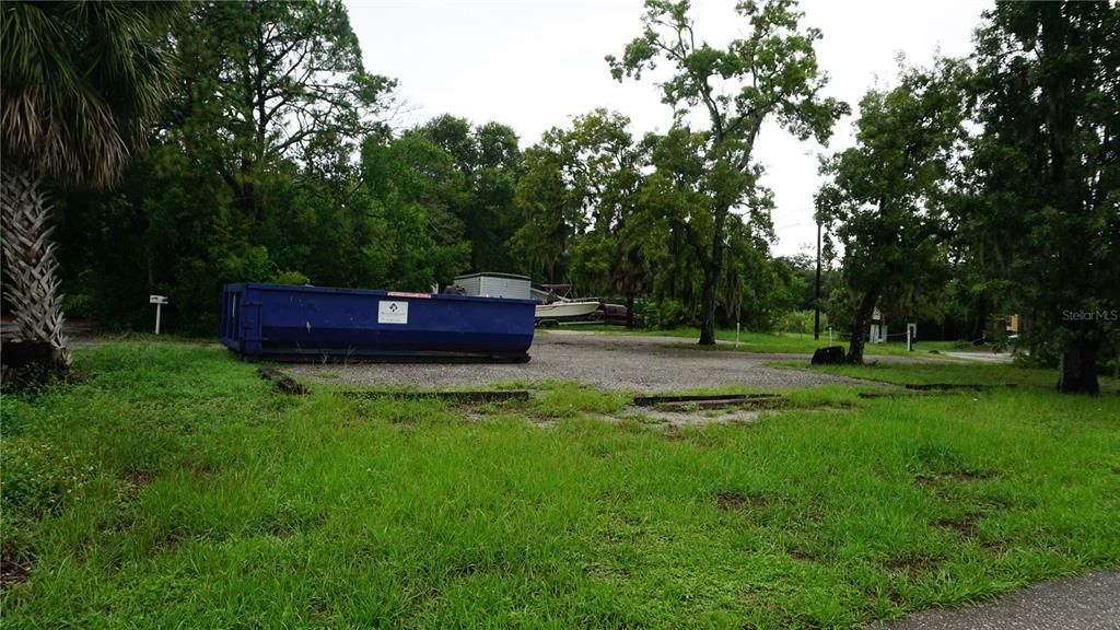 A blue dumpster sits on a gravel lot surrounded by grass and trees — 7317 LITTLE ROAD, NEW PORT RICHEY, FL