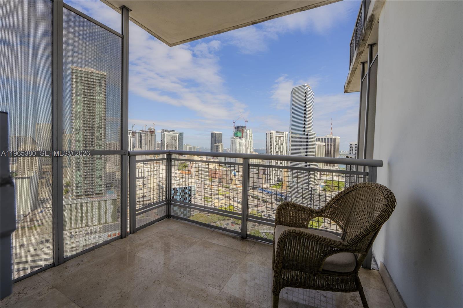 A balcony with a wicker chair overlooks a dense urban skyline with high-rise buildings — 350 S Miami Ave # 3203, Miami FL 33130, MIAMI, FL